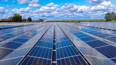 Vista panorámica de un campo de paneles solares fotovoltaicos instalados en un área amplia, bajo un cielo azul con nubes esponjosas.