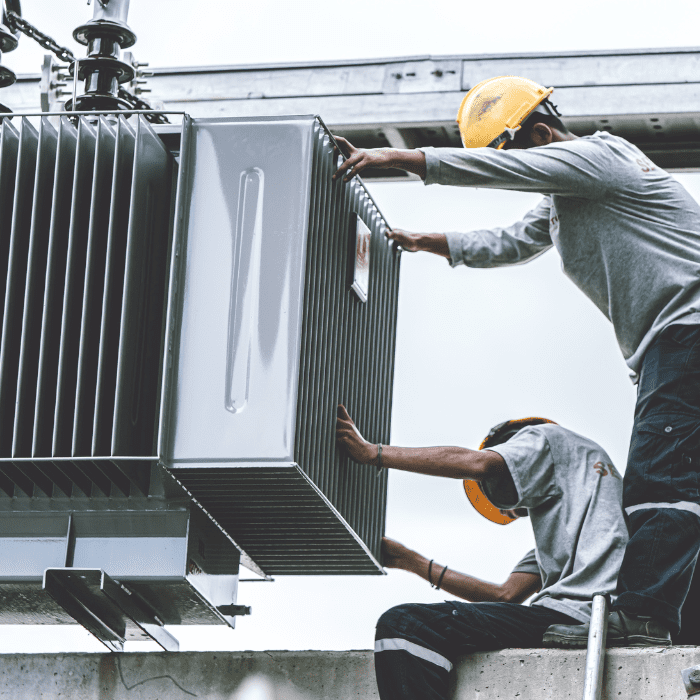 Técnicos Con Cascos De Seguridad Instalando Un Transformador Eléctrico En Una Subestación.