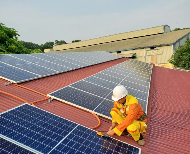 Técnico instalando sistema de paneles solares en techo residencial de lámina roja, con equipo de seguridad.