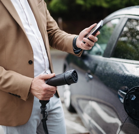 Persona conectando su auto eléctrico mientras revisa su celular durante la carga
