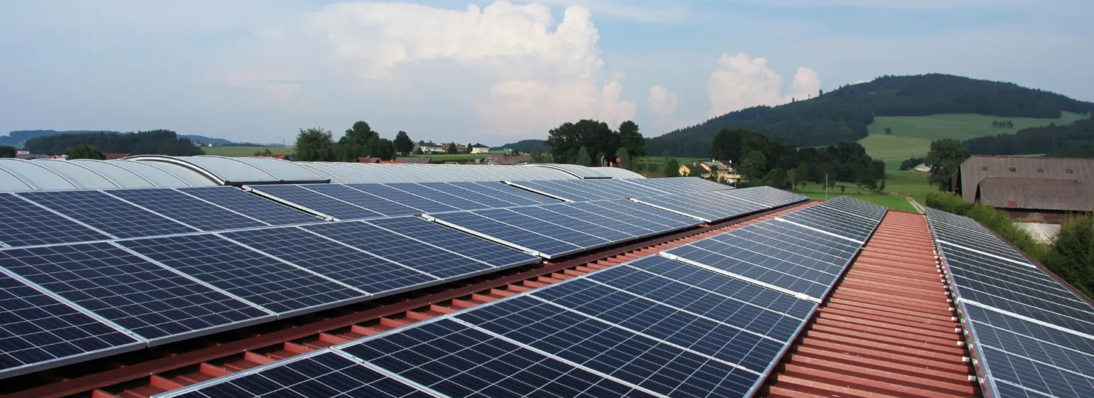 Paneles solares en techo metálico rojo con vista panorámica y nubes al fondo en zona rural