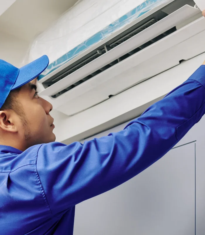 Técnico instalando aire acondicionado tipo minisplit en interior de vivienda con uniforme azul y gorra